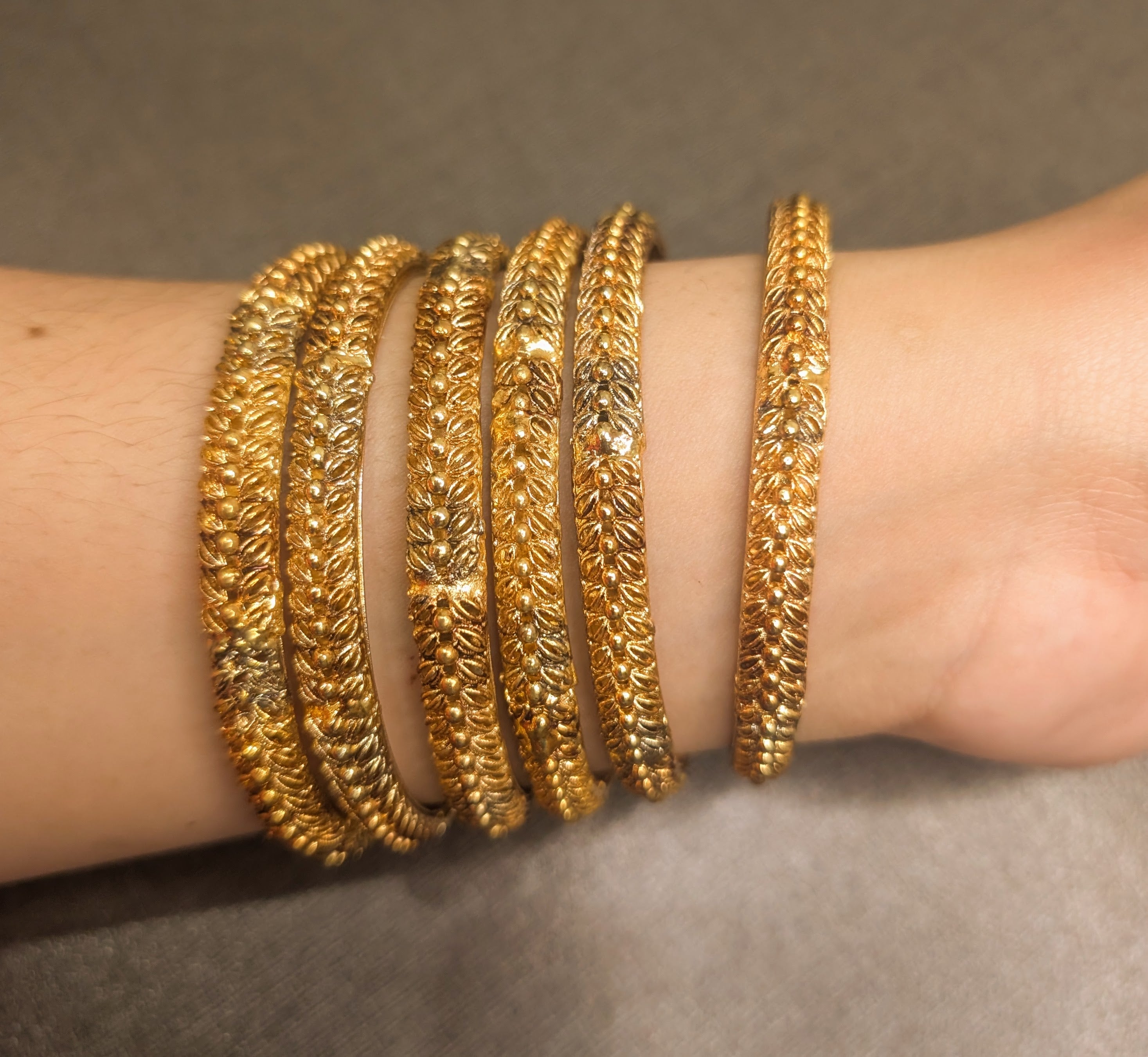 Look like Gold but not gold bracelets on a wrist against a neutral background